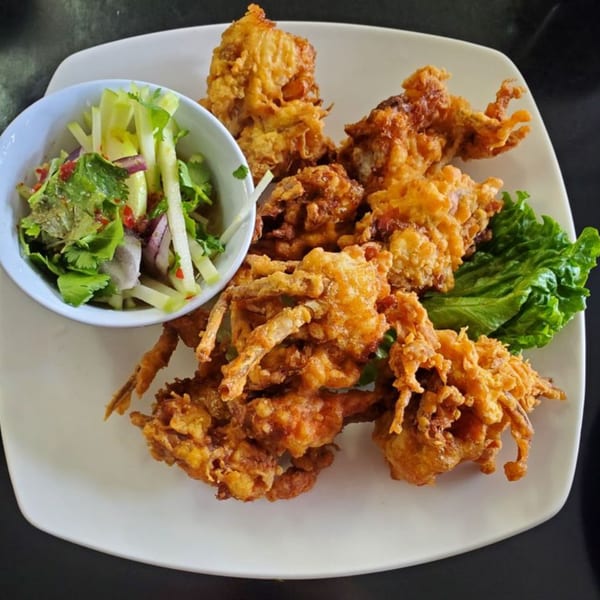 Crispy fried soft-shell crabs with a side of fresh green salad on a white plate.