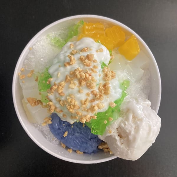 Colorful Thai dessert with shaved ice, blue sticky rice, green jelly, orange fruit, and peanuts.