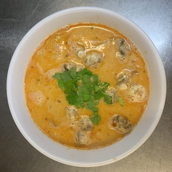 A white bowl of Sapp Coffee Shop's Thai soup with oysters and cilantro on a metal surface.