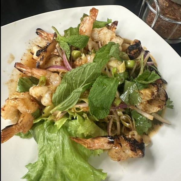 Grilled shrimp salad with fresh mint, red onion, and green vegetables on a white plate.