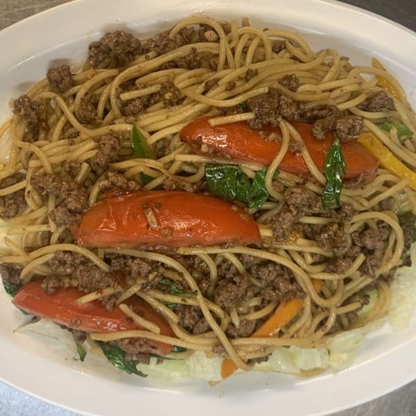 Thai spaghetti with ground beef, red bell peppers, and basil on a white plate.