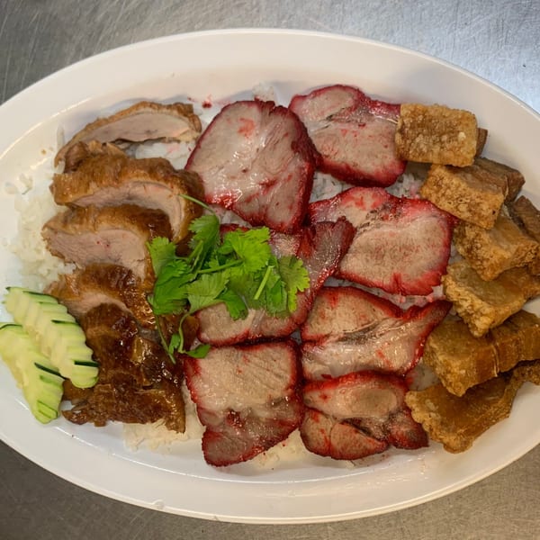 A Thai dish with sliced roasted duck, red pork, crispy pork belly, cilantro, and cucumber over rice.