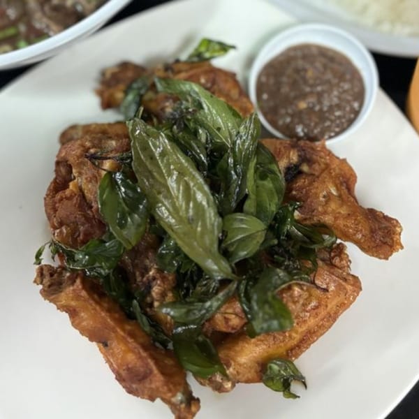 Crispy fried chicken pieces topped with fresh green basil leaves, served with a side of dipping sauce.