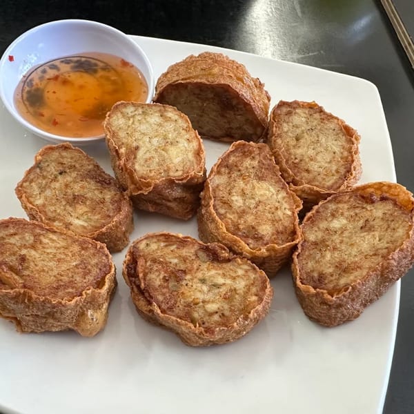 Eight pieces of golden-brown fried Thai shrimp cakes (Tod Mun Goong) with a side of sweet chili sauce.