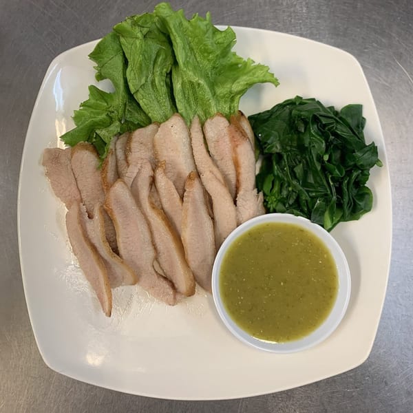 Sliced pork with fresh lettuce, green vegetables, and a side of green dipping sauce.