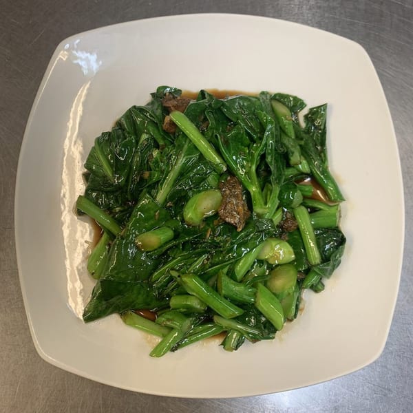 A white square plate filled with stir-fried green vegetables and pieces of meat in a brown sauce.